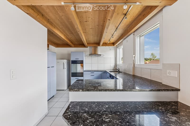 Modern kitchen with granite countertops, white cabinets, stainless steel appliances, and a wooden ceiling with exposed beams.