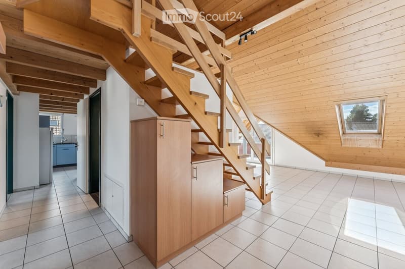 Bright hallway with wooden staircase, white tiled floor, and built-in wooden cabinet. Exposed wooden beams on the ceiling and a window providing natural light.
