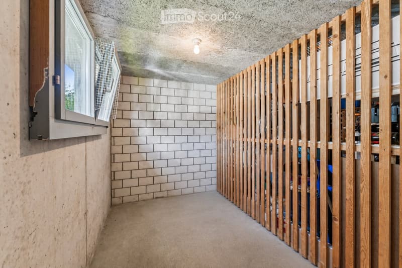 A narrow hallway with a wooden slatted partition on one side, white tiled wall on the other, and a window at the end.