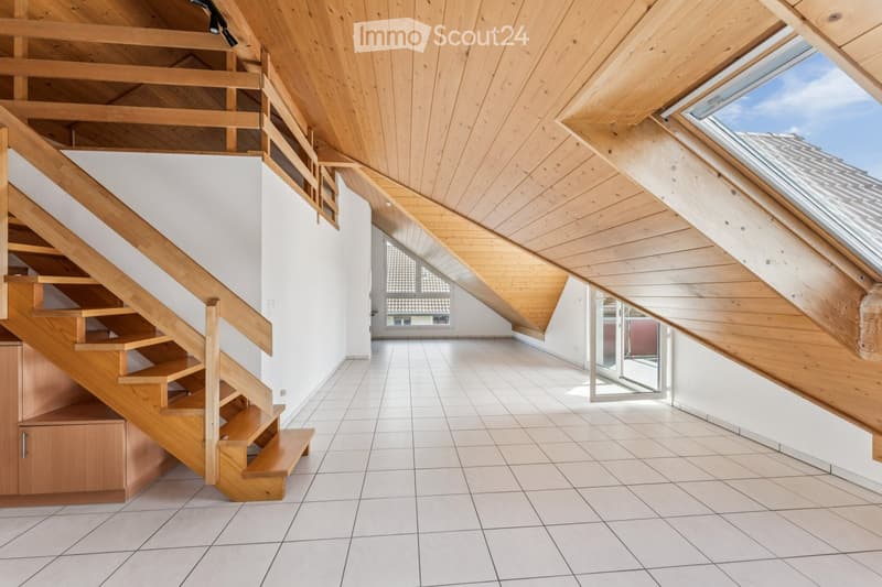 Bright, open attic space with wooden staircase, wooden beams, skylights, and tiled floor.