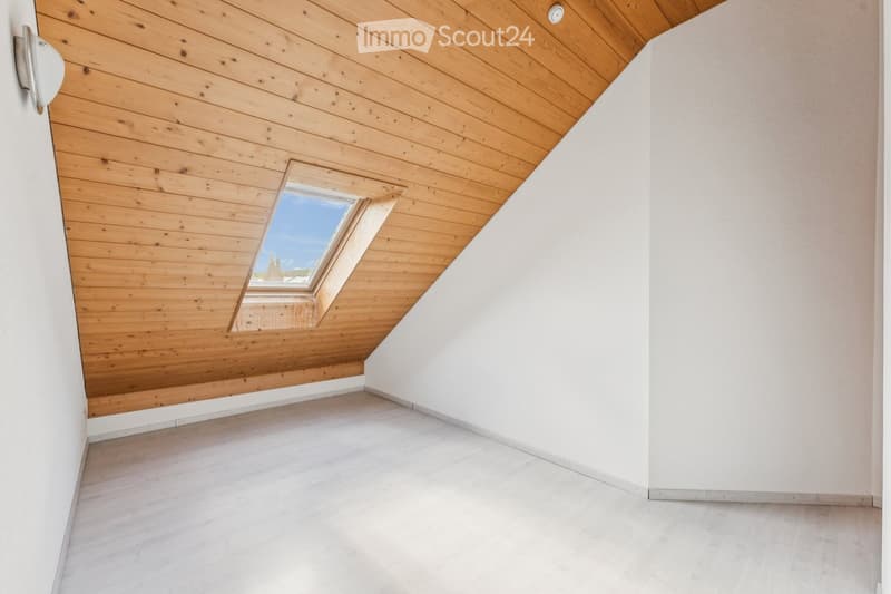 Empty room with wooden ceiling, white walls, and a skylight window. The floor is light-colored and the space is minimalistic with no furniture.