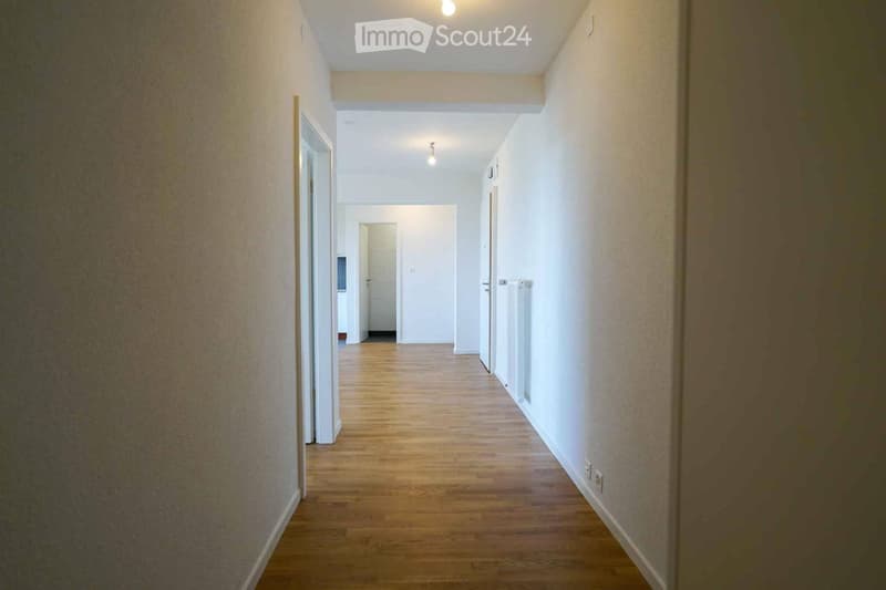 Empty hallway with wooden flooring, white walls, and several doors leading to other rooms.