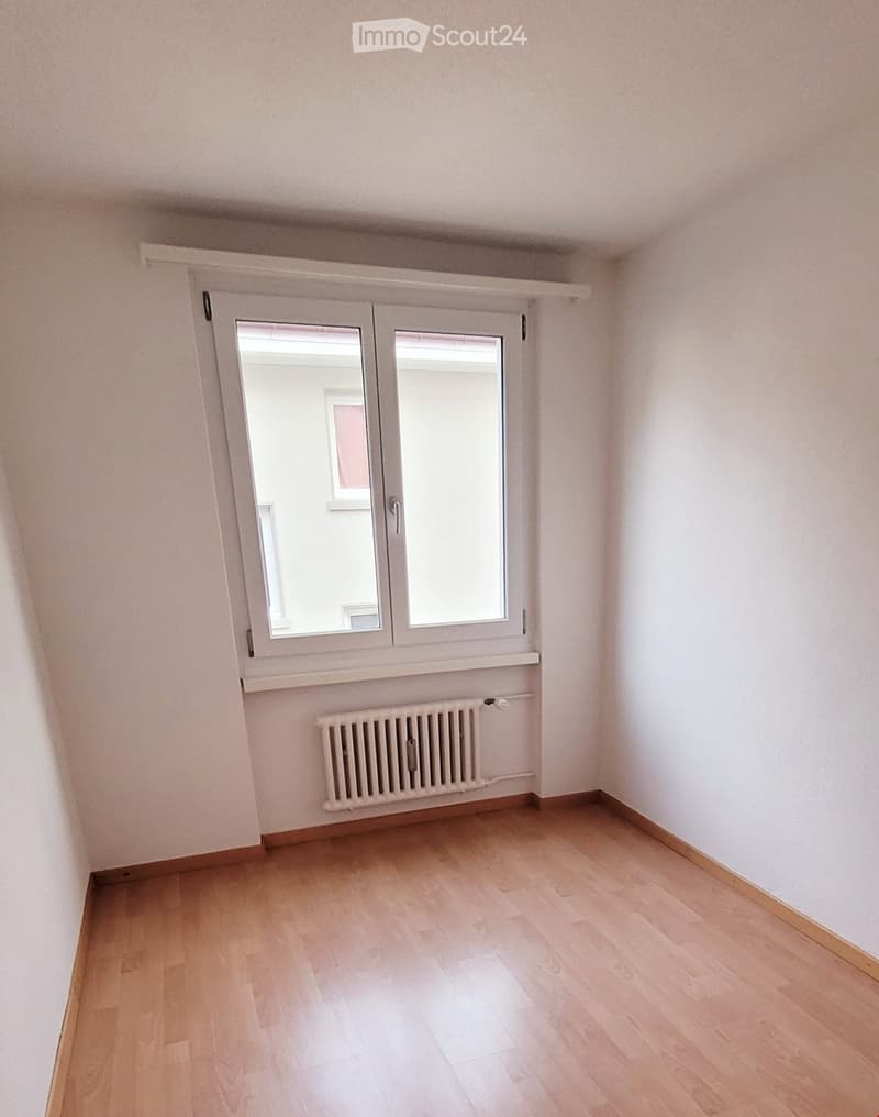 Empty room with light wooden flooring, white walls, a window with white frame, and a radiator below the window.