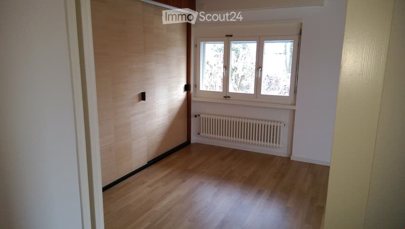 Empty room with wooden flooring, white walls, and a window with three panes. A radiator is placed below the window.