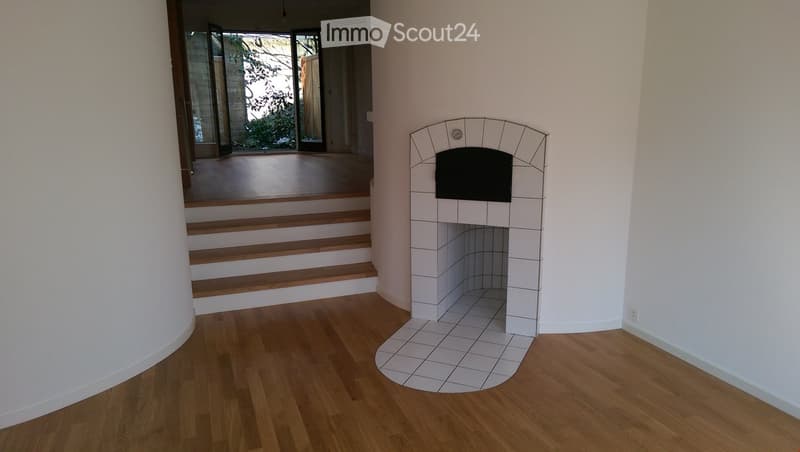 A modern hallway with wooden flooring, a built-in fireplace with a tiled surround, and a staircase leading to another level.