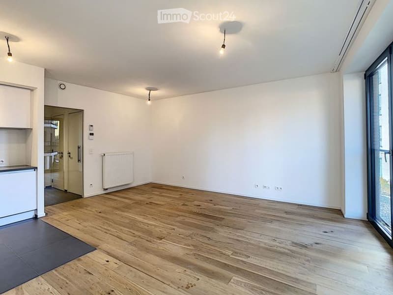 Completely empty room with wooden flooring, white walls, and large windows. No furniture or equipment present.