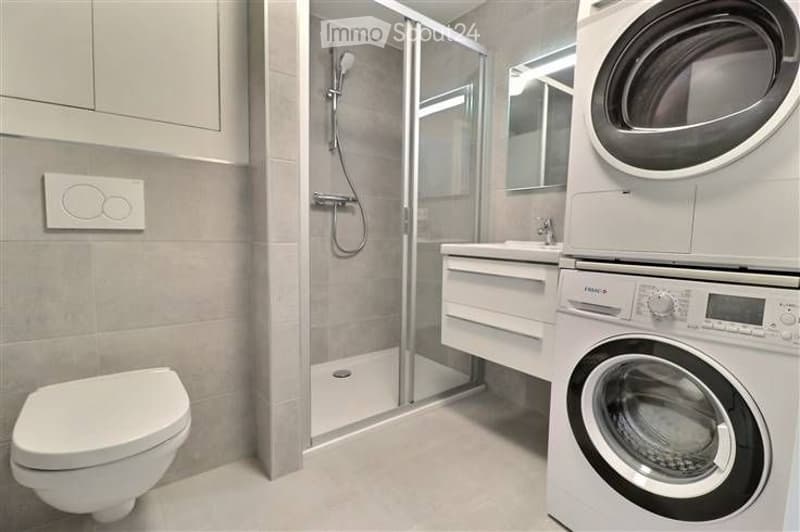 Modern bathroom with a toilet, sink, glass-enclosed shower, and a stacked washer/dryer unit.