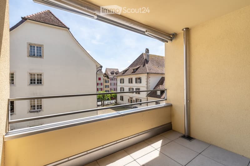 Balcony with tiled floor, metal railing, and a view of neighboring buildings and rooftops.