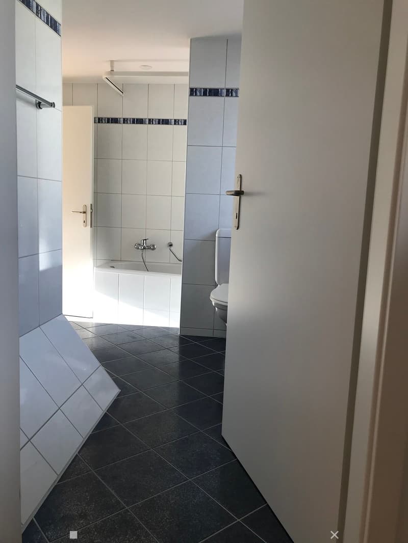 Modern bathroom with white tiled walls, dark tiled floor, bathtub, toilet, and a faucet.