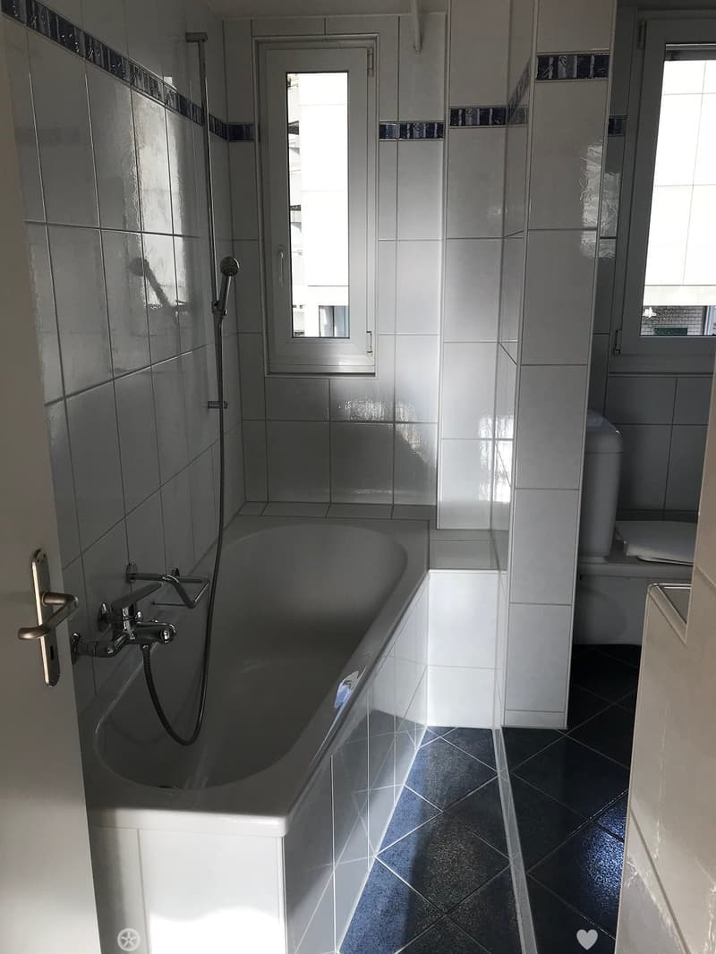 Modern bathroom with a bathtub, toilet, and showerhead, featuring white tiled walls and black tiled floor.