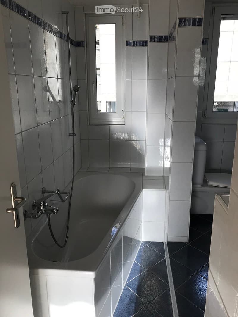 Modern bathroom with a bathtub, toilet, and showerhead, featuring white tiled walls and black tiled floor.