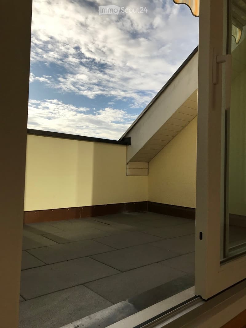 A small, tiled balcony with a slanted roof and a view of the sky.