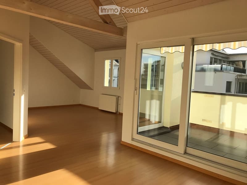 Empty room with wooden flooring, large windows, and a slanted wooden ceiling. No furniture or equipment present.