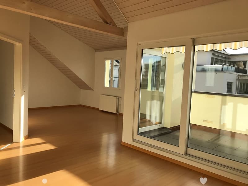 Empty room with wooden flooring, large windows, and a slanted wooden ceiling. No furniture or equipment present.