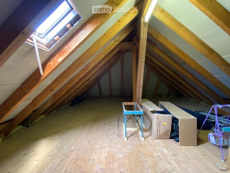 Empty attic space with wooden beams, wooden floor, skylight window, and some cardboard boxes and a small table.