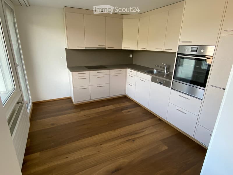 Modern kitchen with light-colored cabinets, wooden flooring, stainless steel appliances including an oven and dishwasher, and a sink with a faucet.