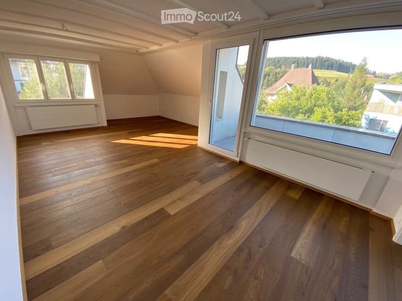 Empty room with wooden flooring, large windows, and a sliding glass door leading to a balcony.