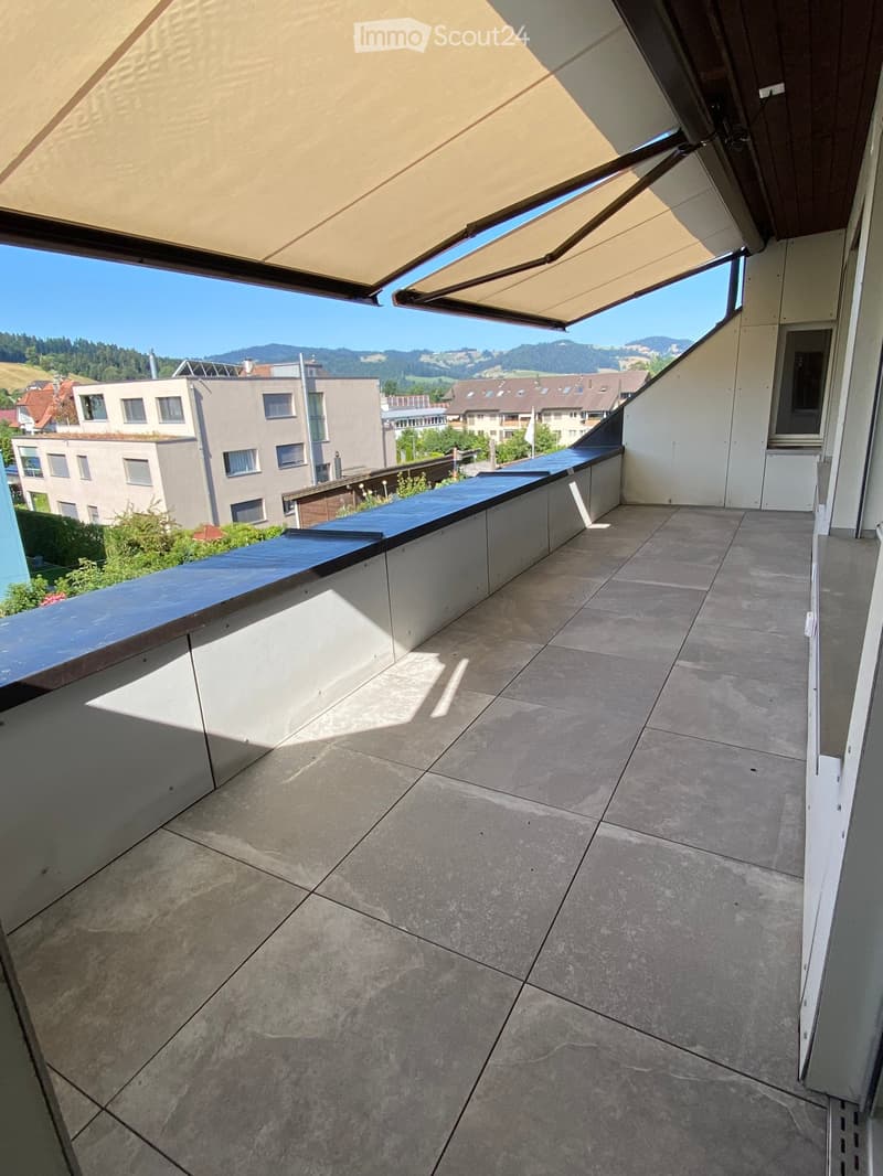 Balcony with tiled floor, modern railing, and retractable awning, overlooking a residential area with buildings and greenery.