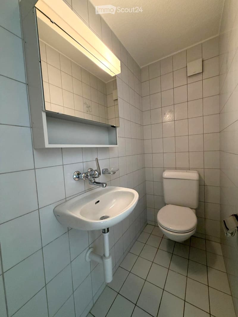 small bathroom with white tiles, white sink, white toilet, mirror, and a soap dish