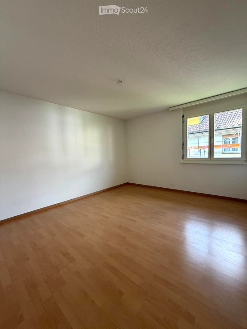 Empty room with white walls, wooden floor, and a window with a view of a building under construction.