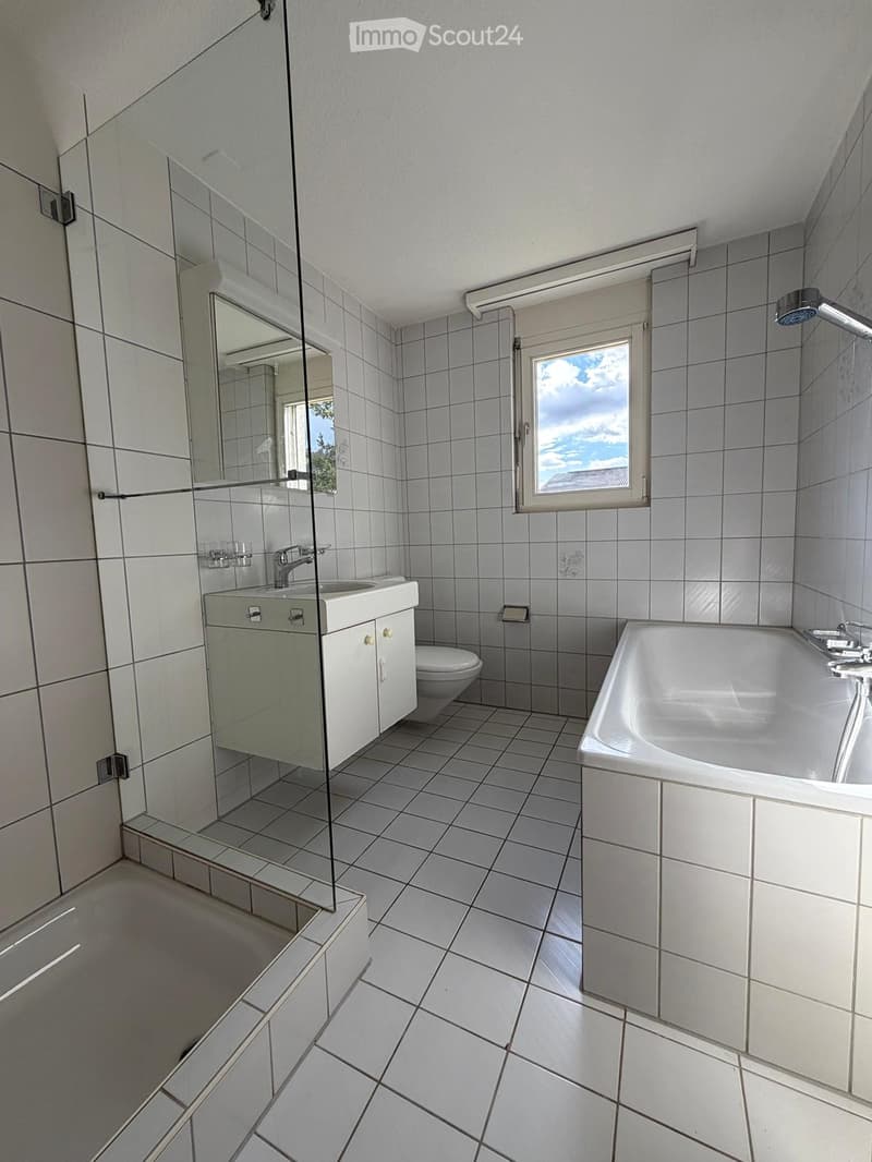 Bathroom with white tiles, glass shower enclosure, white bathtub, white sink, mirror, toilet, and window