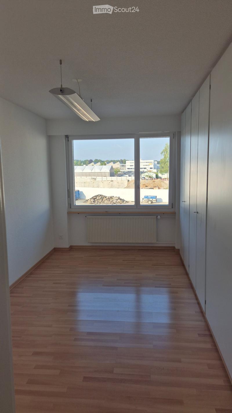 Empty room with wooden flooring, white walls, large window, radiator, and overhead lighting fixture.