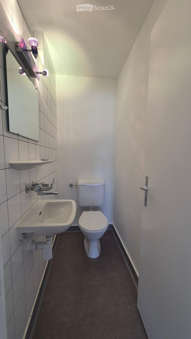 Modern bathroom with white tiled walls, a toilet, a sink, and a mirror with built-in lighting.