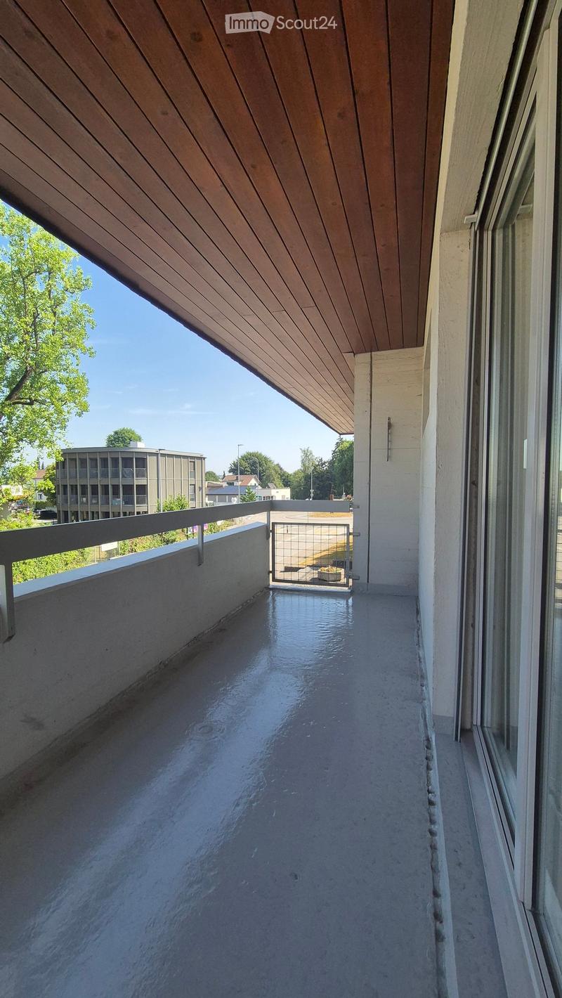Modern balcony with wooden ceiling, concrete floor, metal railing, and a small gate leading to a small outdoor area.