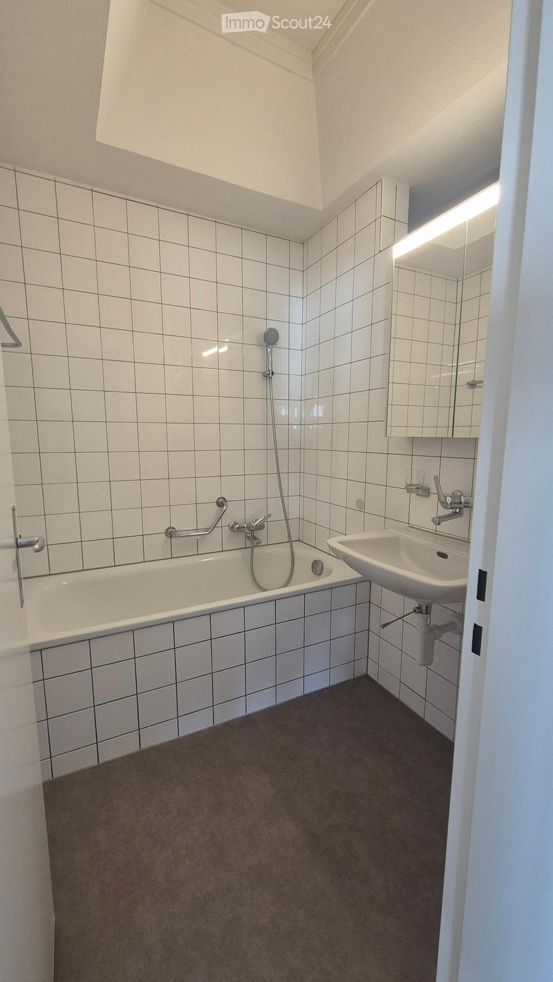 Modern bathroom with white tiled walls and floor, featuring a bathtub, sink, and mirror.