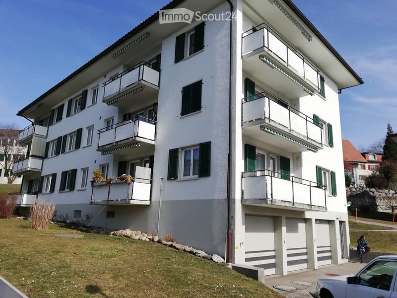 A multi-story residential building with white exterior, green shutters, multiple balconies, and a garage at the base.