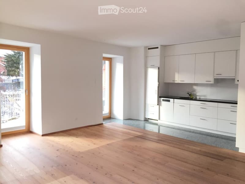 Modern kitchen with white cabinets, a refrigerator, and a dishwasher. The space features wooden flooring and large windows offering a view of the outdoors.