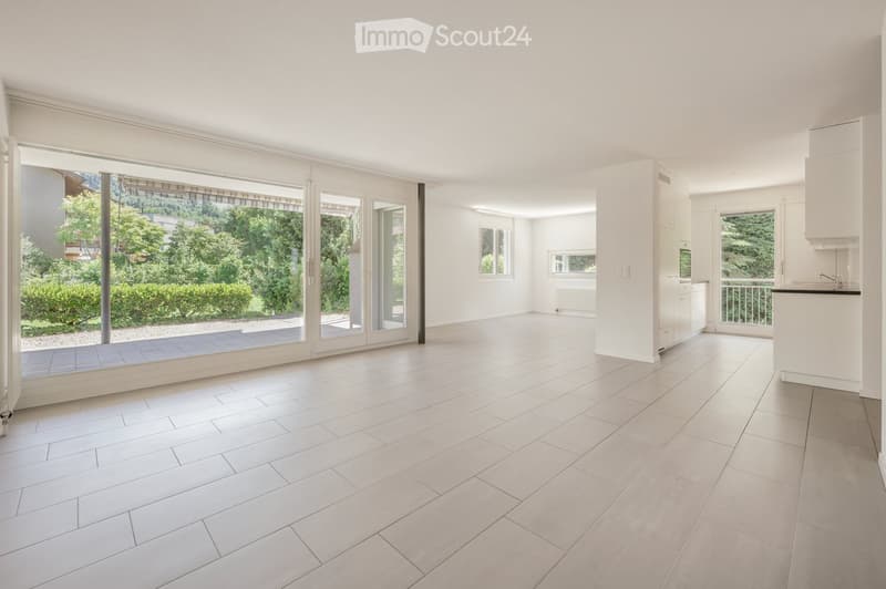 Bright, empty room with large sliding glass doors leading to a balcony, white tiled floor, white walls, and built-in kitchen cabinets.