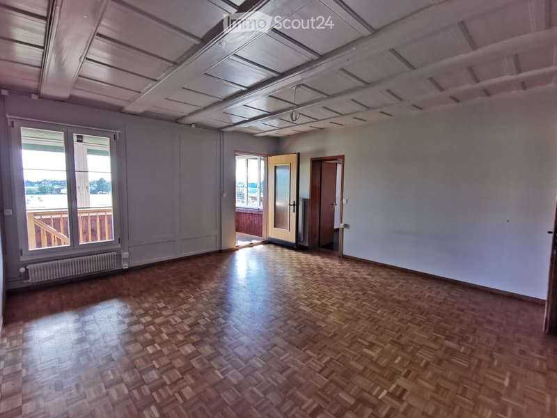 Empty room with wooden parquet flooring, white walls, large windows, and a balcony access. No furniture or equipment present.