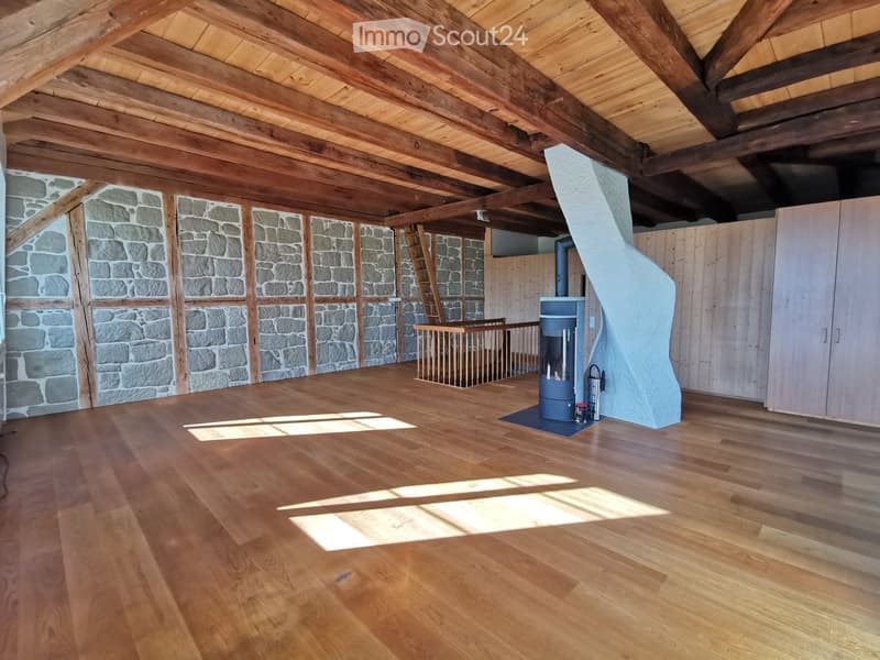 Empty room with wooden flooring, exposed wooden beams, stone walls, and a staircase leading to an upper level. No furniture or equipment is present.