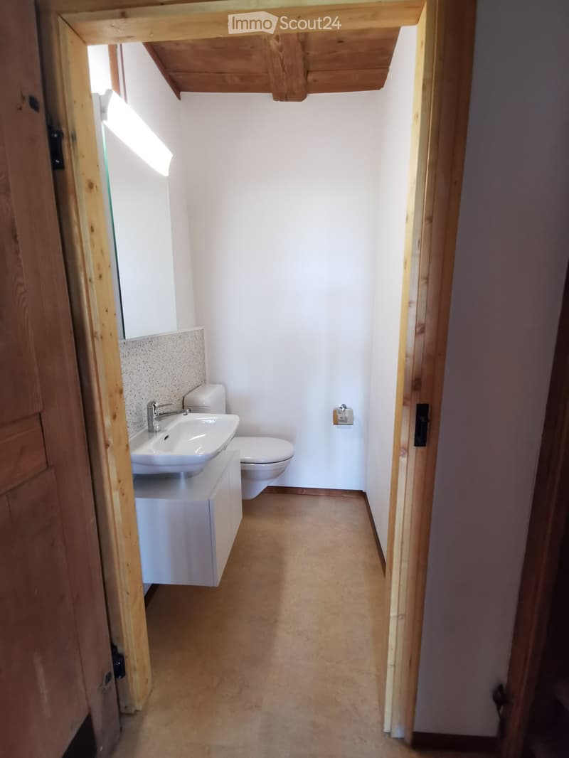 Modern bathroom with white walls, beige tiled floor, white sink with chrome faucet, toilet, and a built-in cabinet.