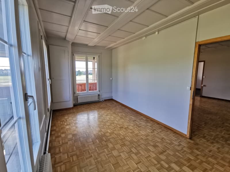 Empty hallway with wooden herringbone flooring, light blue walls, and large windows allowing natural light. There are doors and a radiator visible.