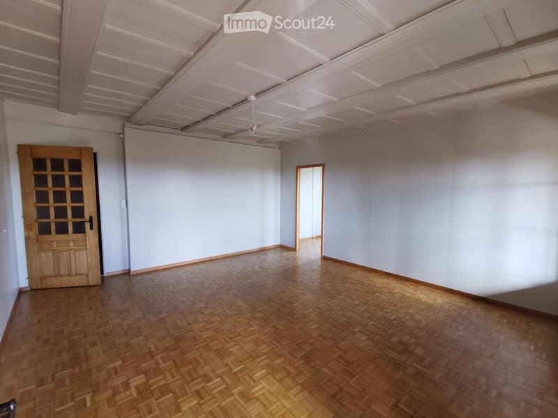 Empty room with wooden parquet flooring, white walls, and a wooden door with glass panels.
