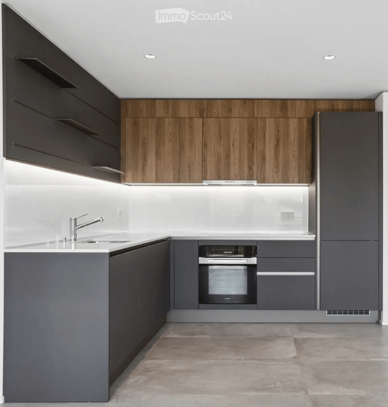 Modern kitchen with sleek grey and dark wood cabinets, a built-in oven, and a stainless steel sink with a modern faucet.