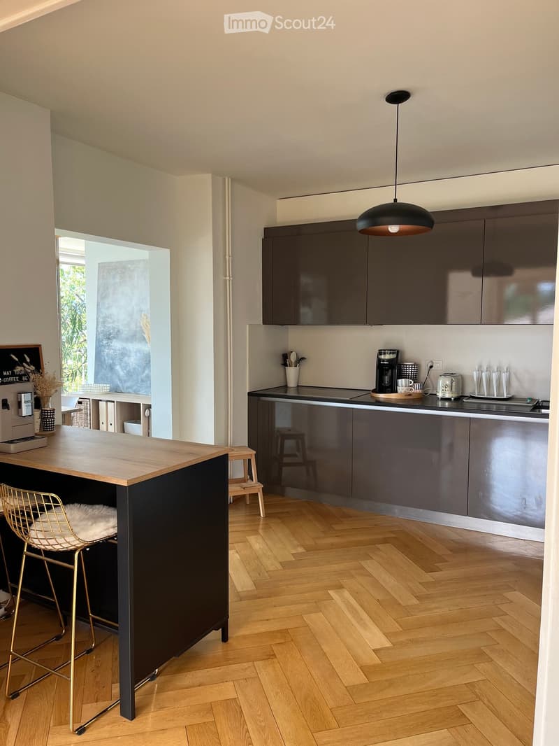 Modern kitchen with dark grey cabinets, wooden herringbone flooring, a central island with a wooden countertop, and a pendant light hanging above.