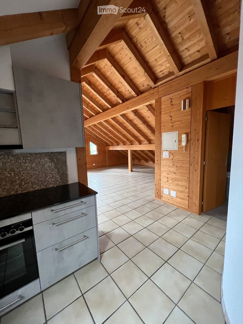 Modern kitchen with grey cabinets, stainless steel oven, and tiled floor, connected to an attic space with wooden beams and exposed rafters.