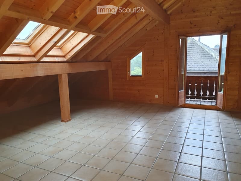 Empty attic space with wooden walls, exposed wooden beams, skylights, and a tiled floor. An open doorway leads to a balcony with a decorative railing.
