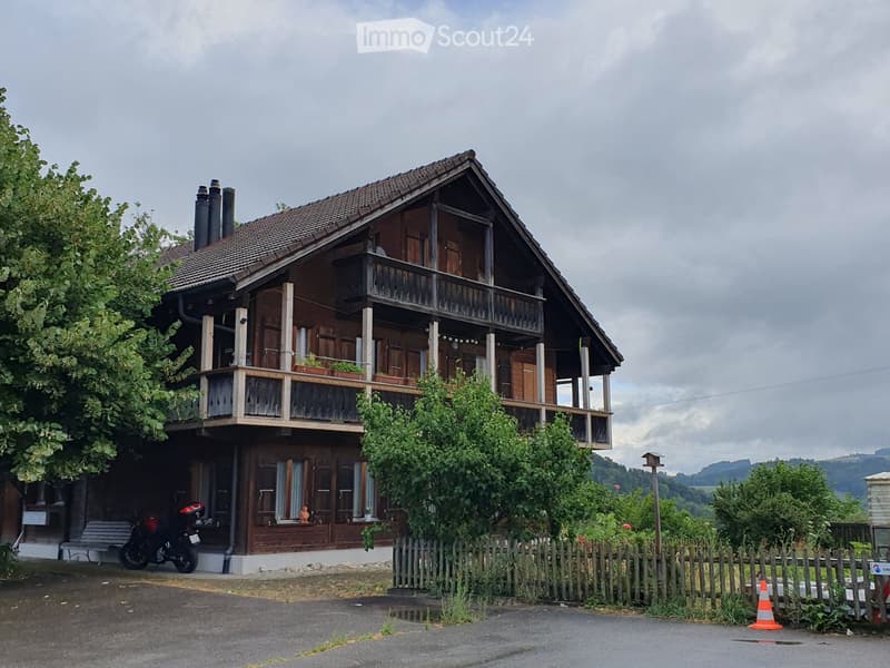 Two-story wooden house with a balcony, multiple windows, and a motorcycle parked in the driveway.