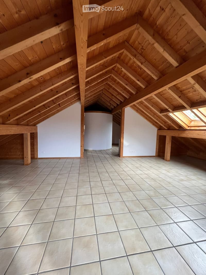 An attic space with exposed wooden beams and slanted ceilings, featuring tiled flooring and skylights, with a cylindrical white object in the center.