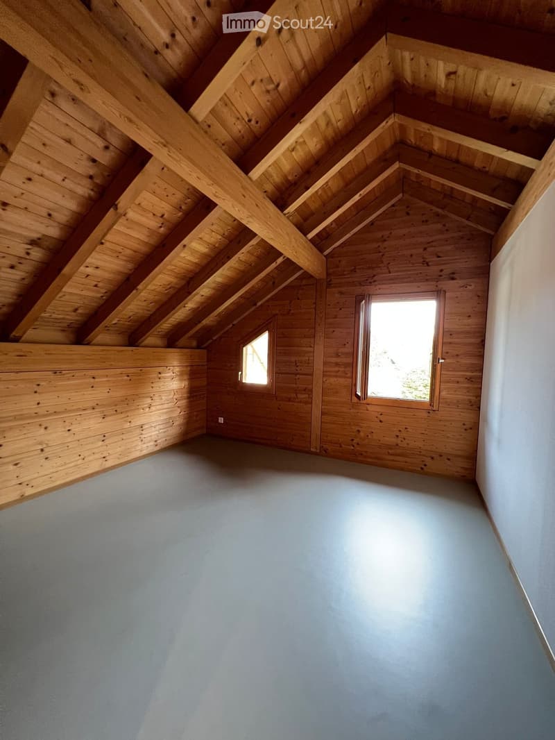 Empty attic space with wooden walls and ceiling, two windows, and a light blue floor.