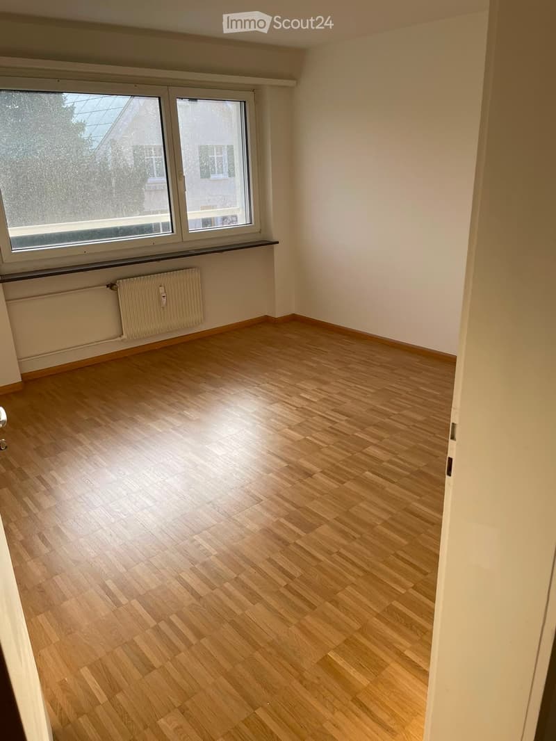 Empty room with wooden flooring, white walls, and large windows with a radiator below them.