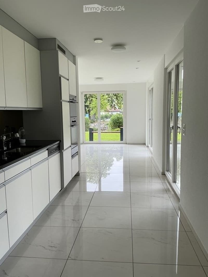 Bright, modern hallway with white walls, polished tile flooring, and large glass doors leading to a garden view.