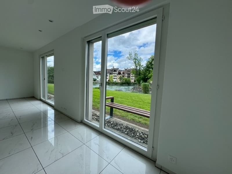 Empty room with white tiled flooring and large sliding glass doors opening to a green outdoor area.