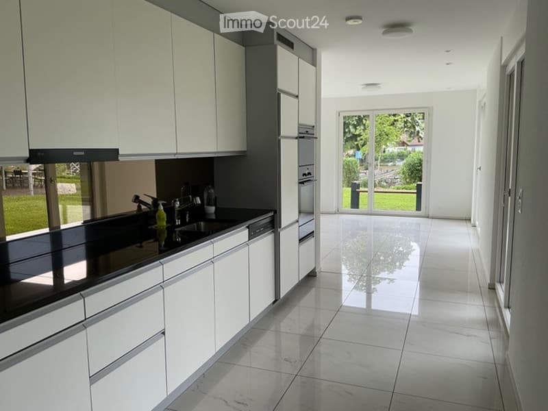 Modern kitchen with white cabinets, black countertops, and a large window offering a view of the garden.