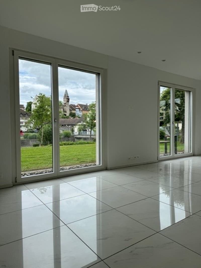 Empty room with large sliding glass doors, white tiled floor, and natural light from the windows.