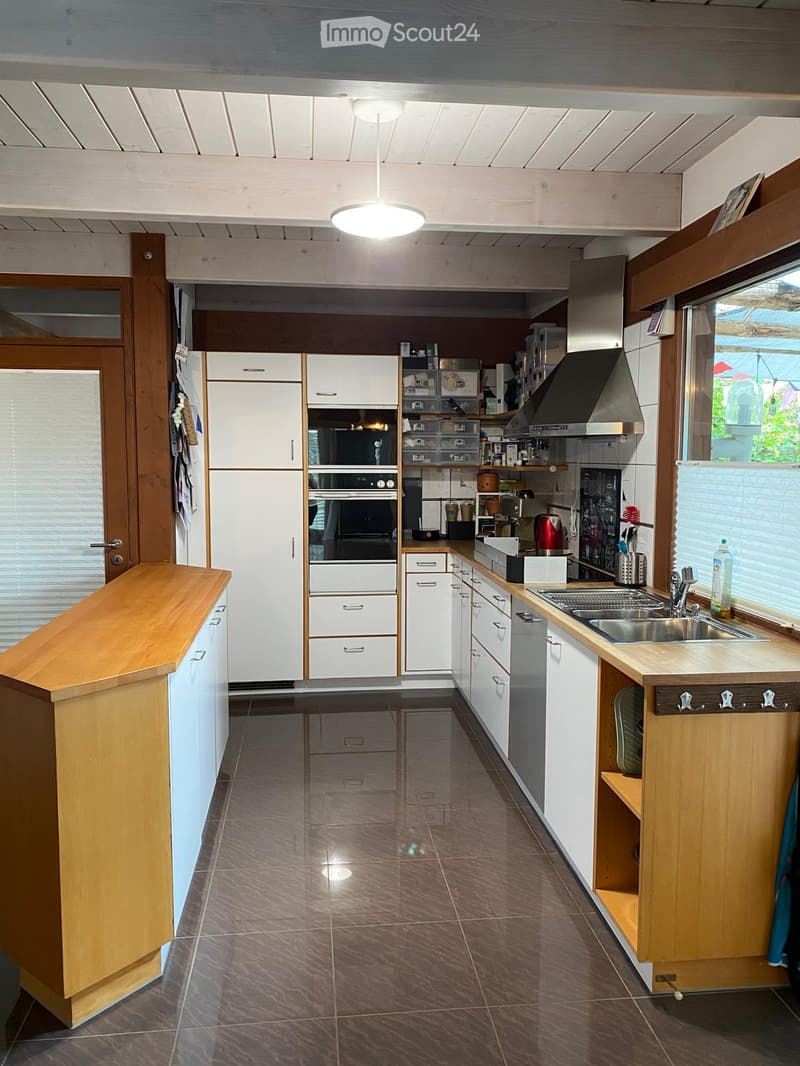 Modern kitchen with white cabinets, stainless steel appliances, wooden island, and large windows.